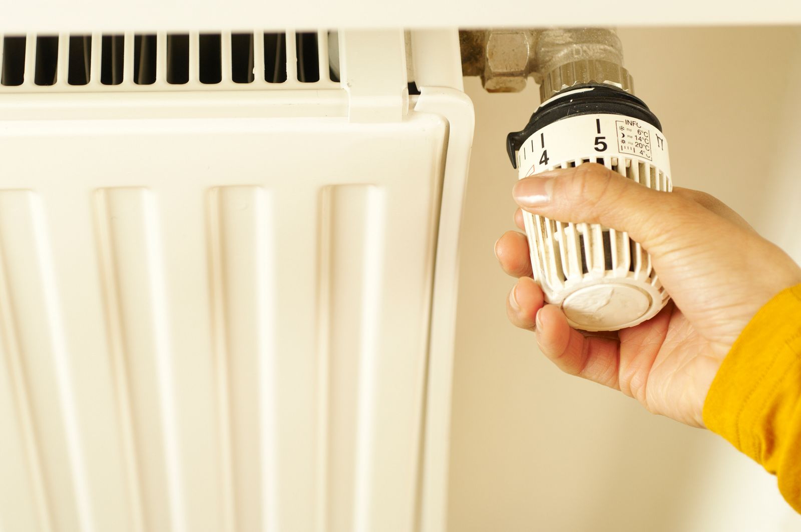 Main réglant une tête thermostatique sur un radiateur dans une maison chauffée et connectée